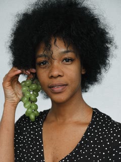 A woman with curly natural hair in a polka-dot top, holding green grapes